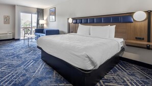 Habitación de hotel con una cama grande, escritorio, silla, balcón y vistas al exterior.