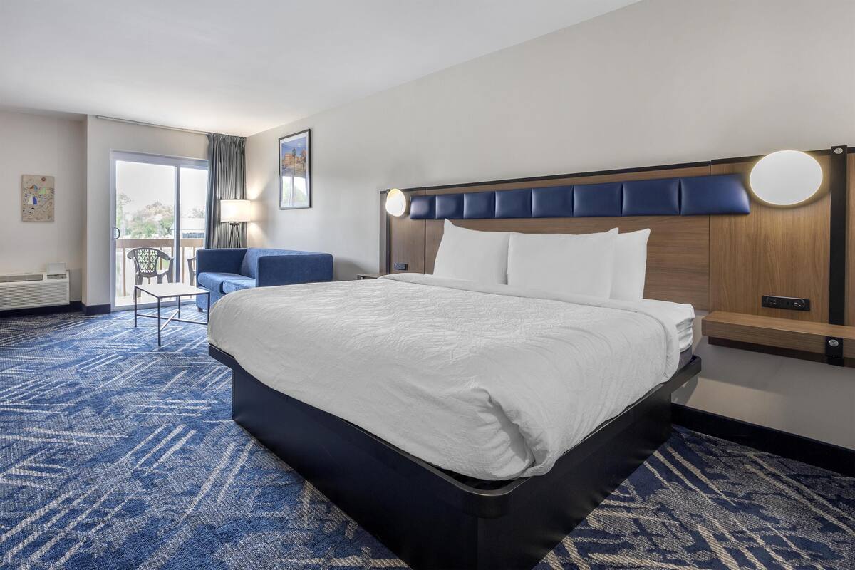 A hotel room with a large bed, a desk, a chair, a balcony, and a view of the outdoors.
