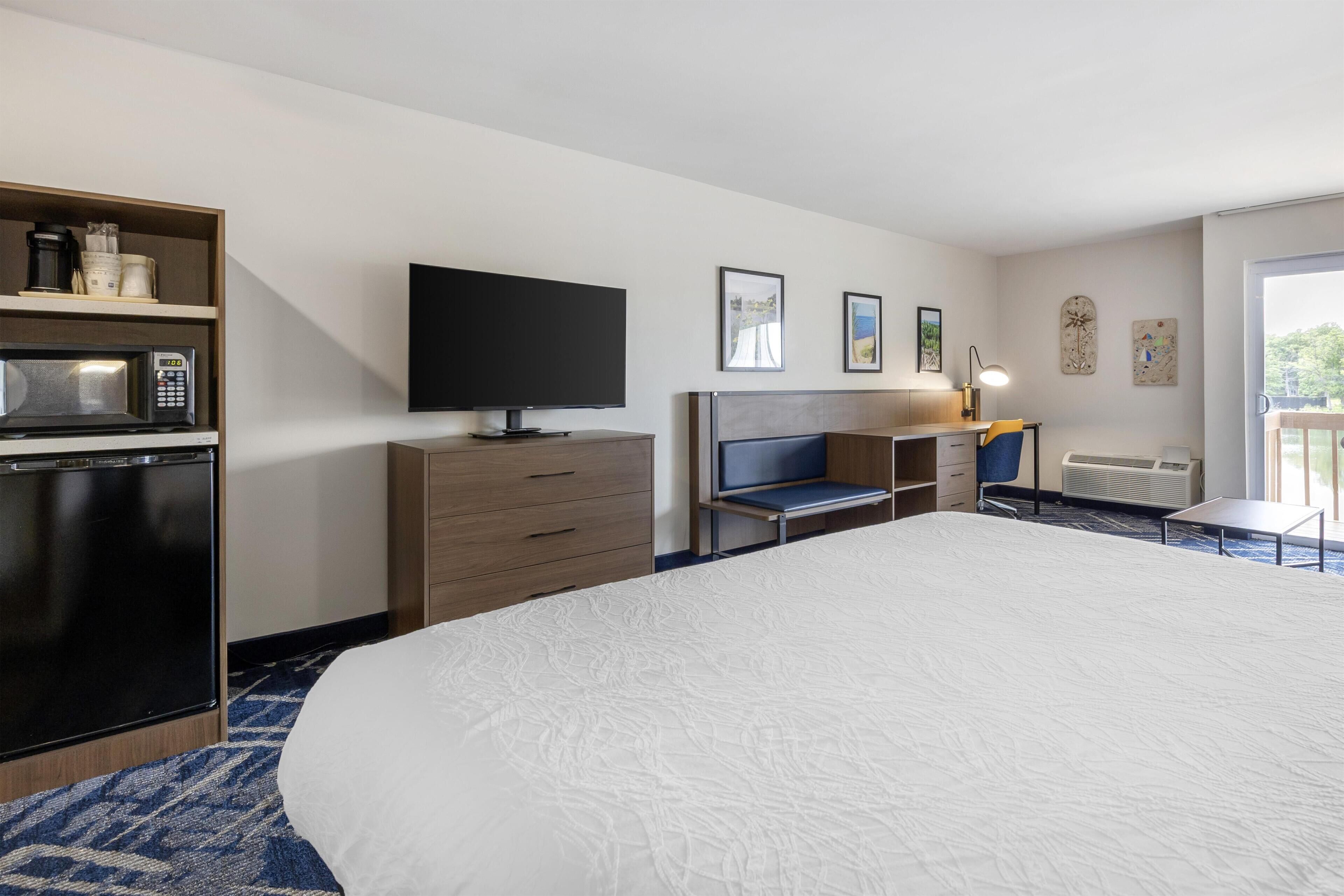 A hotel room with a bed, a television, a desk, a chair, a microwave, a mini-fridge, and a balcony with a view.