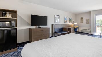 A hotel room with a bed, a television, a desk, a chair, a microwave, a mini-fridge, and a balcony with a view.