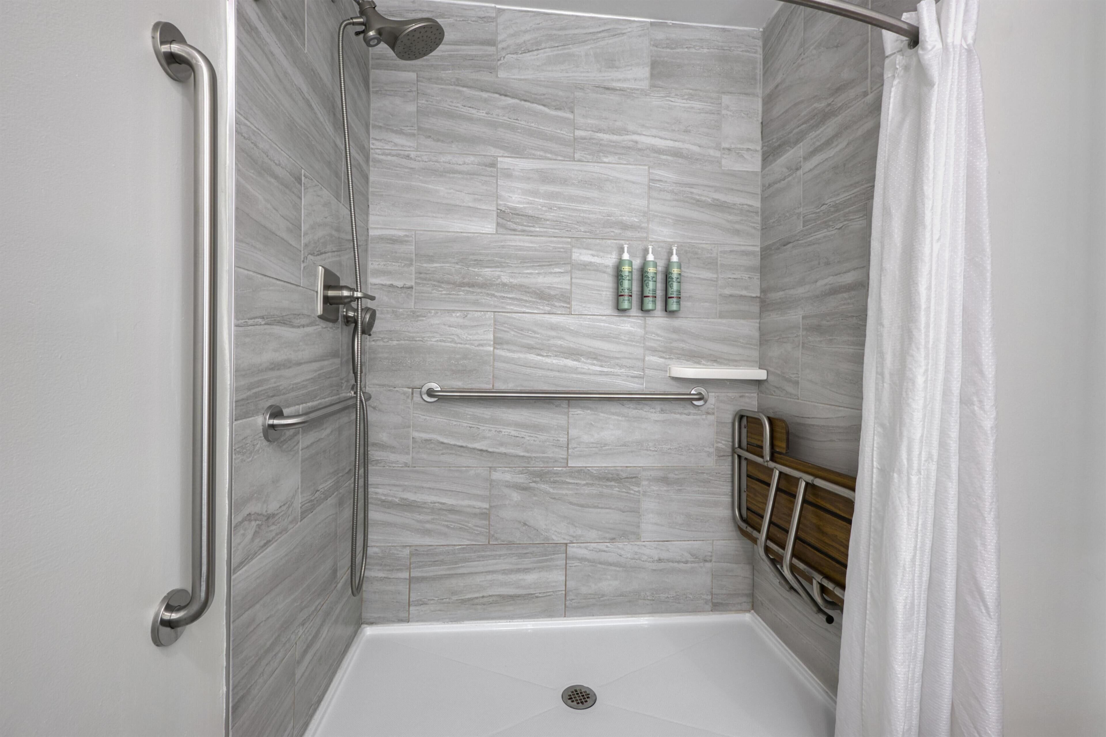 A shower with a grab bar, a shelf with toiletries, and a wooden bench.