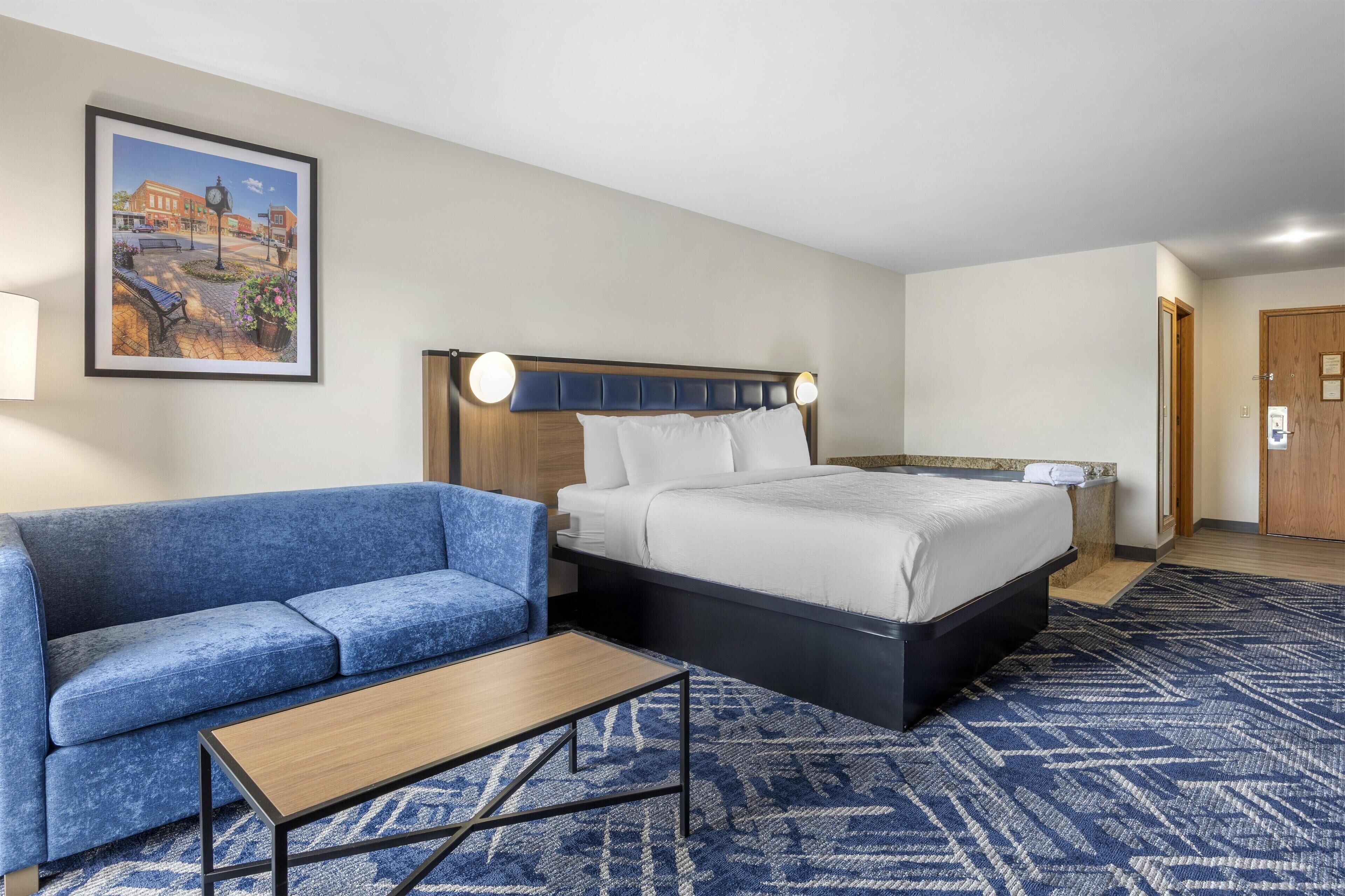 Quarto de hotel com uma cama, um sofá azul, uma mesinha e um quadro na parede.