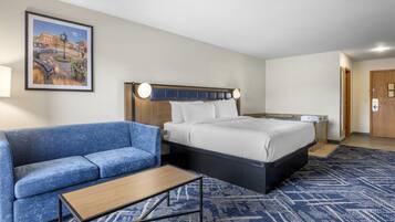 Quarto de hotel com uma cama, um sofá azul, uma mesinha e um quadro na parede.