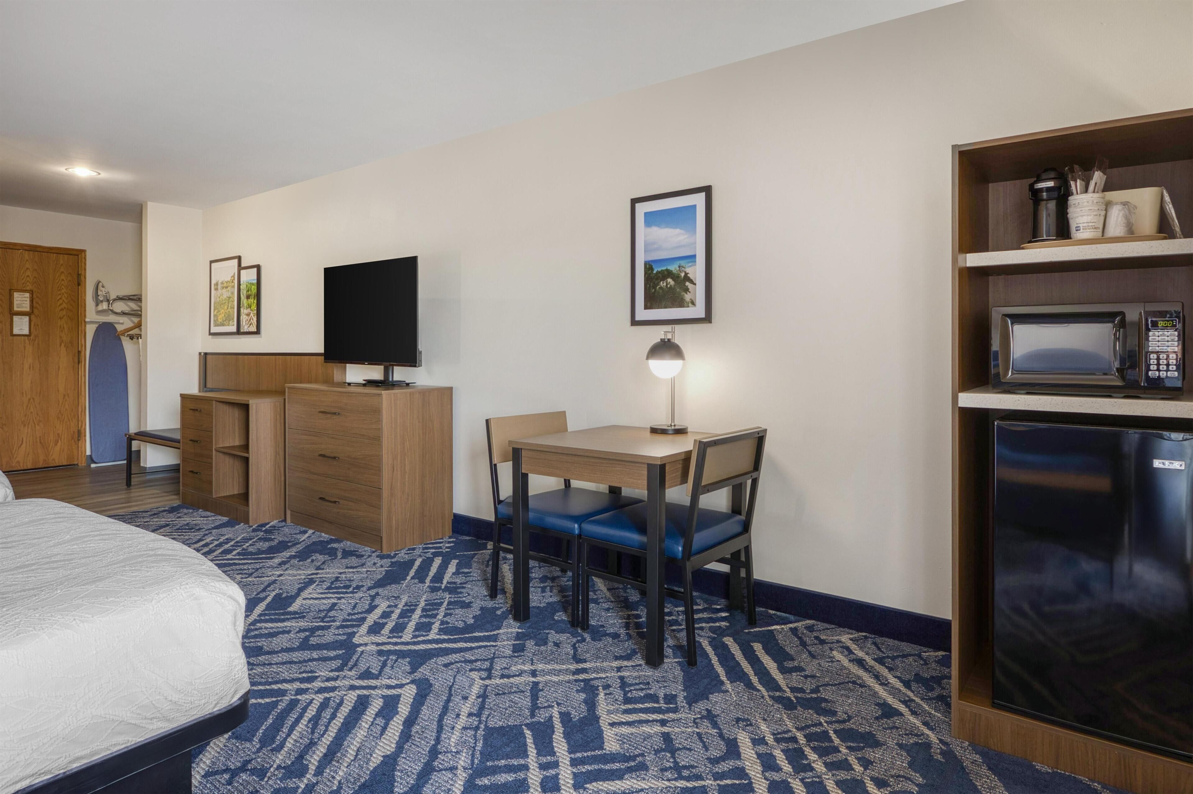 A hotel room with a bed, a desk with a chair, a television, a microwave, and a refrigerator.