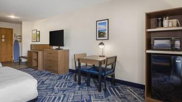 A hotel room with a bed, a desk with a chair, a television, a microwave, and a refrigerator.