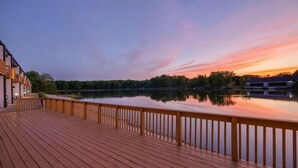 Una terraza de madera con barandilla que da a un lago tranquilo al atardecer.