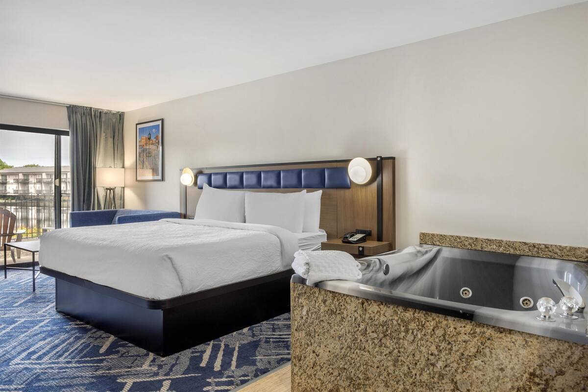 A hotel room with a bed, a bathroom with a bathtub, a desk, and a chair.