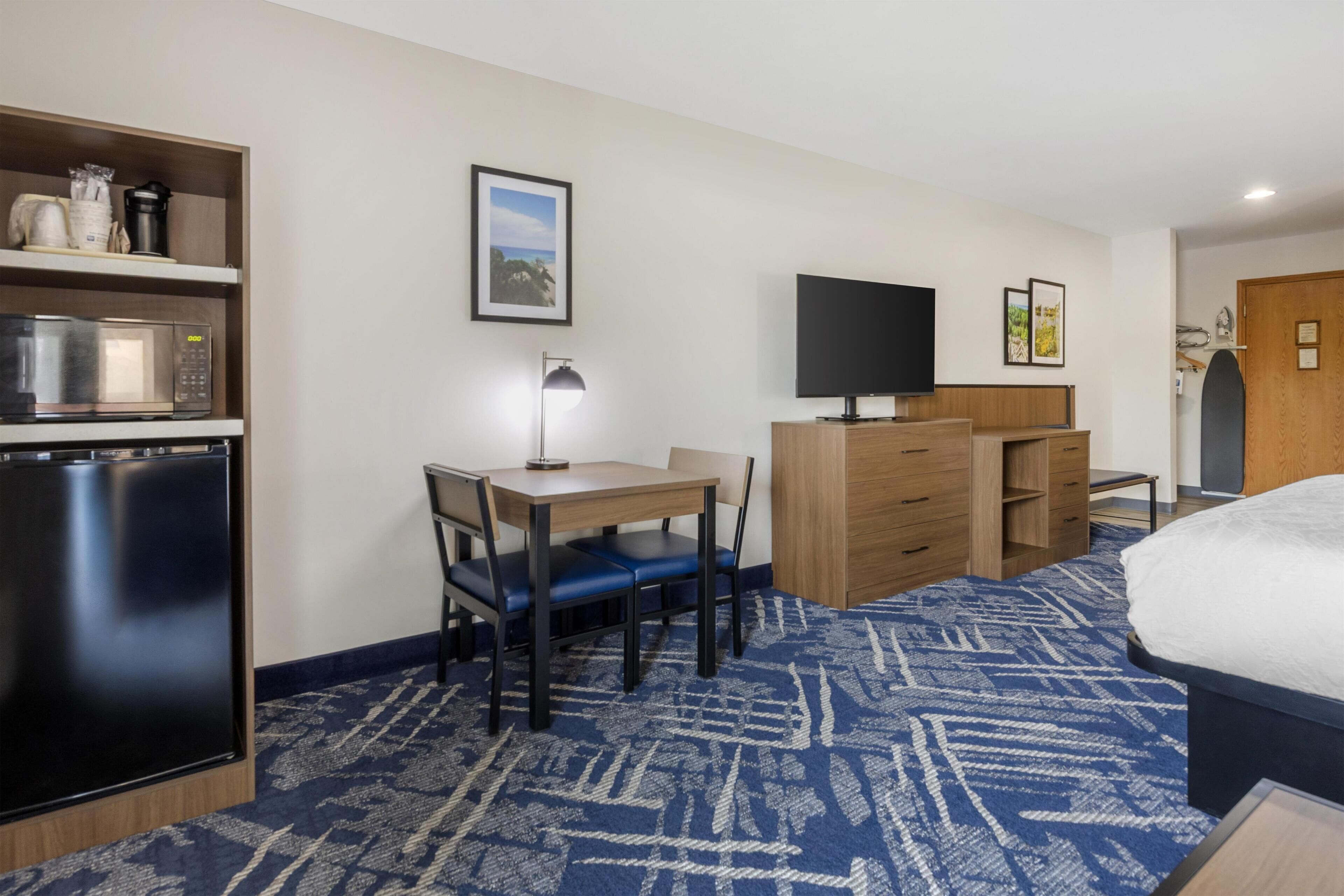 A hotel room with a bed, a desk with a chair, a microwave, a refrigerator, a flat-screen TV, and a wardrobe.