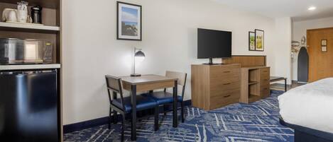 A hotel room with a bed, a desk with a chair, a microwave, a refrigerator, a flat-screen TV, and a wardrobe.