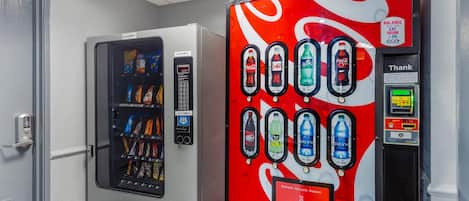 Máquina expendedora con diversas bebidas y aperitivos, una máquina de Coca-Cola y una interfaz de pago digital.