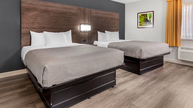 A hotel room with two beds, a wooden headboard, a wall-mounted light, and a window with curtains.