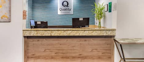 Un mostrador de recepción de hotel con un cartel que dice 'Quality by Choice Hotels', una pantalla digital y una planta.