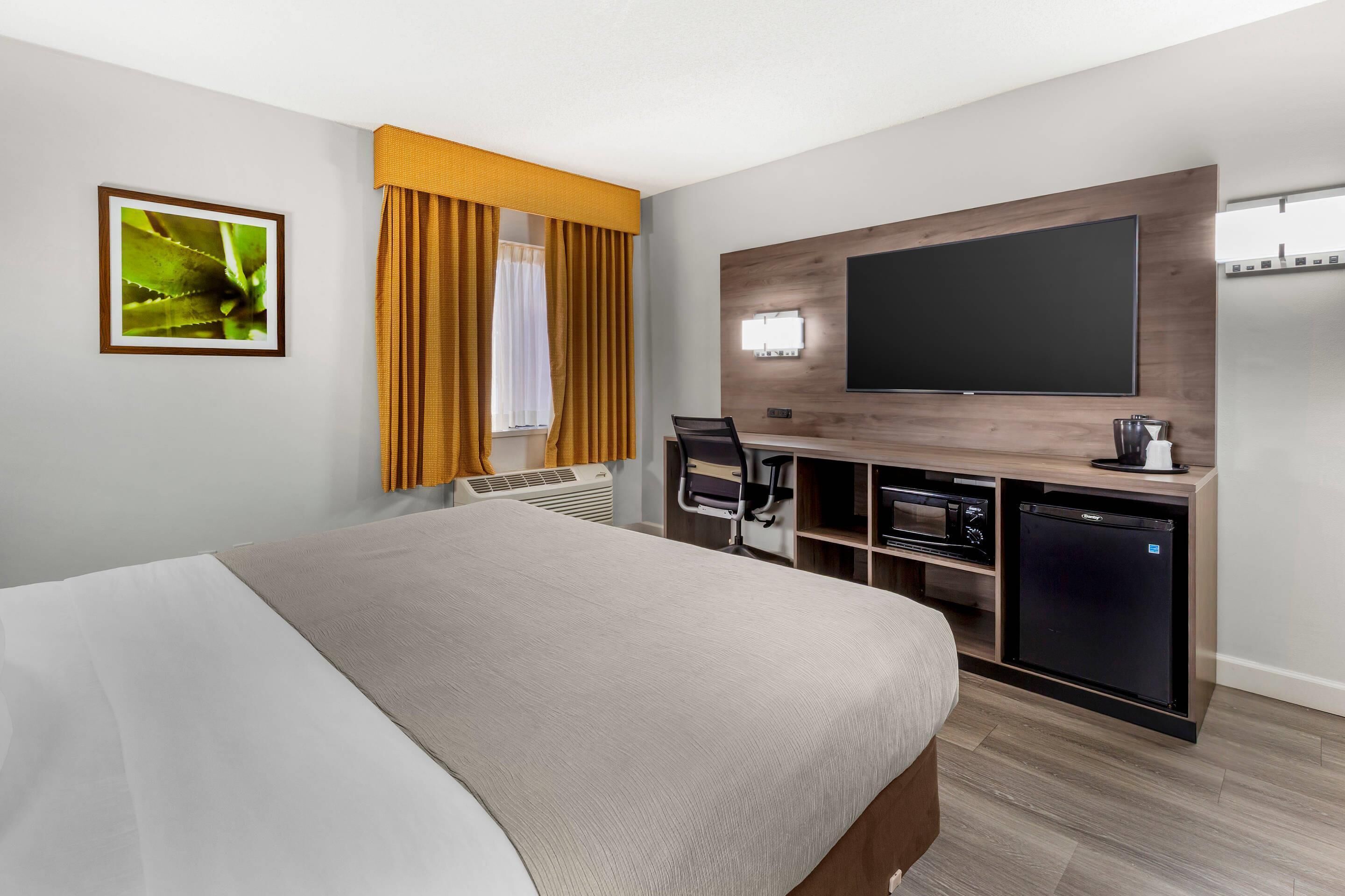 A hotel room with a bed, a desk with a flat-screen TV, a mini-fridge, and a microwave.