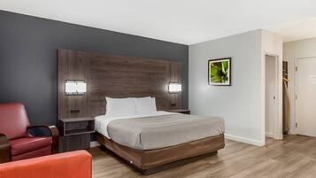Una habitación de hotel con una cama grande, dos mesitas de noche con lámparas, un sillón rojo y un cabecero de madera.