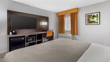 A hotel room with a large bed, a flat-screen TV mounted on the wall, a desk with a chair, a small refrigerator, and a microwave.