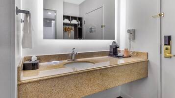 A bathroom with a granite countertop sink, a mirror, a towel rack, and a shower area visible through the glass door.