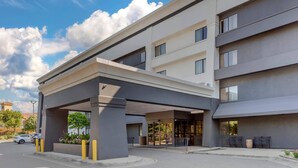 A modern hotel entrance with a covered walkway, multiple floors, and a parking area.