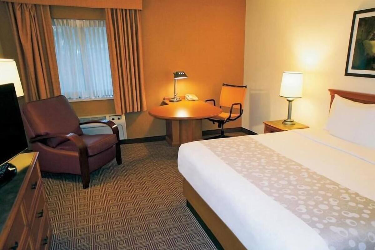 A hotel room with a bed, a desk with a lamp, a chair, and a window with curtains.