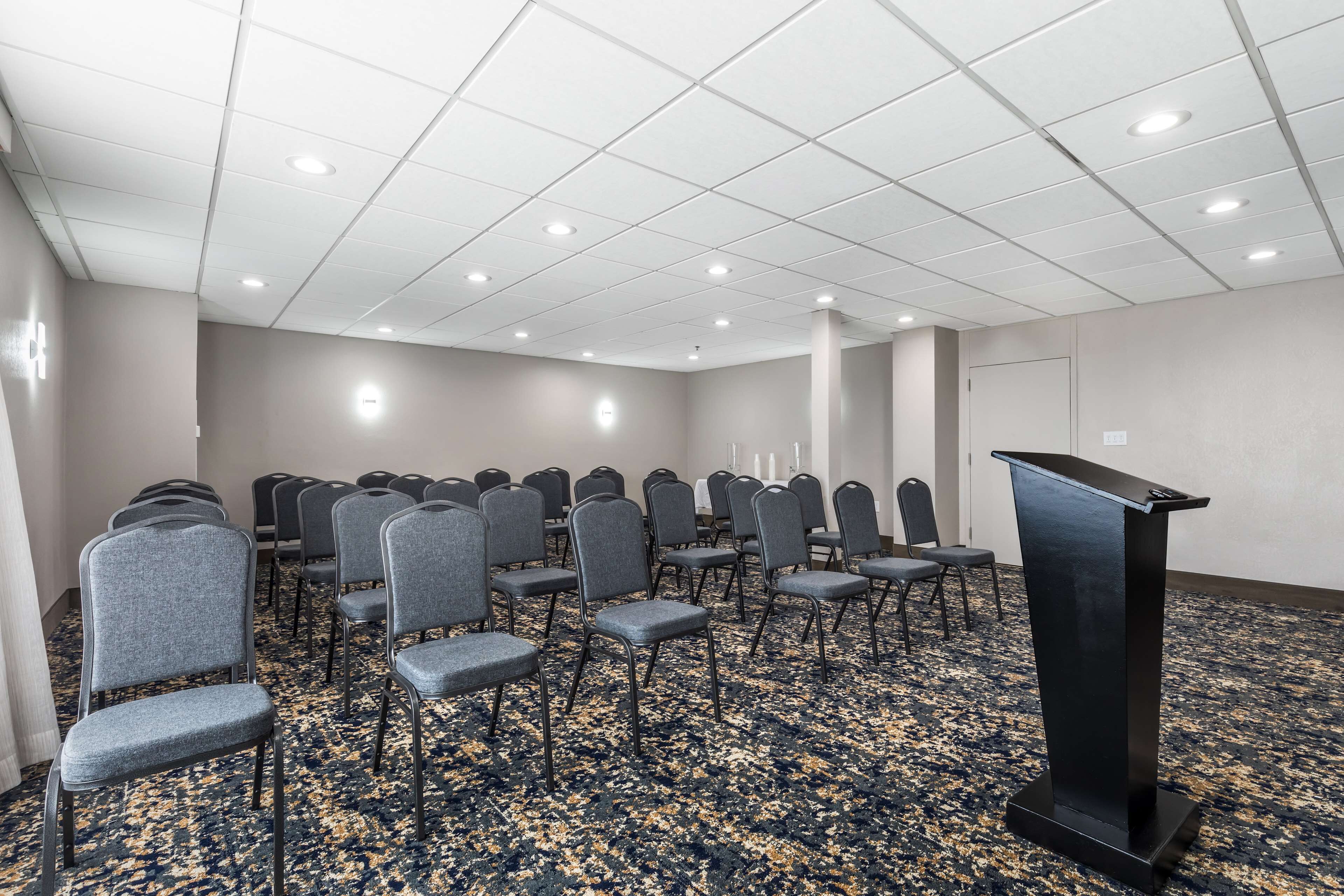 A conference room with rows of chairs, a podium, and a carpeted floor.