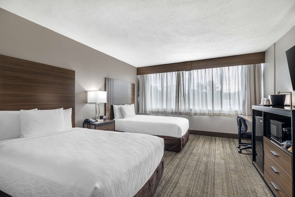 A hotel room with two beds, a desk with a computer, a TV, and a window with curtains.