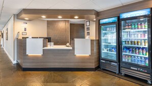 Zona de recepción con diseño moderno, que incluye un mostrador de recepción, un panel informativo en la pared y un refrigerador con bebidas.