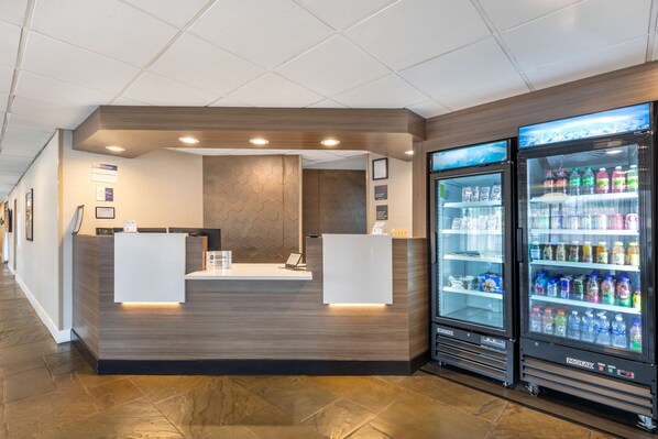 A reception area with a modern design, including a reception desk, a wall-mounted information board, and a refrigerator stocked with beverages.