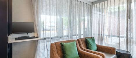 A modern room with a brown sofa, a TV on a stand, and sheer curtains.