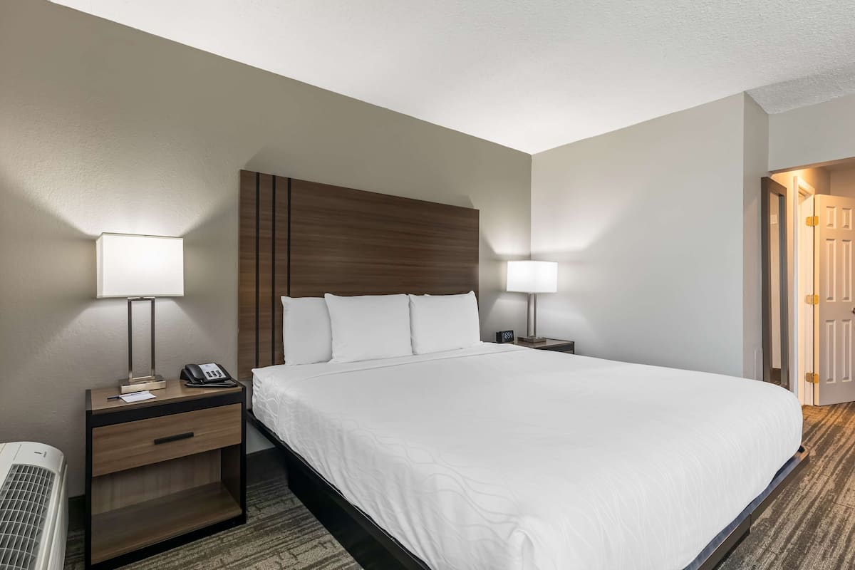 A hotel room with a large bed, two bedside tables with lamps, a heater, and a door to the right.