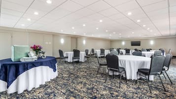 A conference room with round tables and chairs, a carpeted floor, and a white ceiling with recessed lighting.