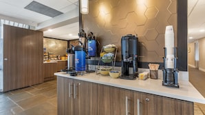 Un área de cocina moderna con una estación de café que incluye varias cafeteras y una pila de vasos desechables.