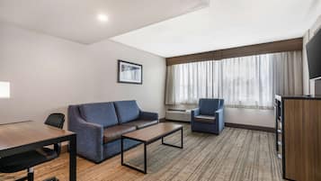 Une chambre d’hôtel moderne avec un bureau en bois, un canapé bleu, une petite table basse et un téléviseur posé sur une commode en bois.