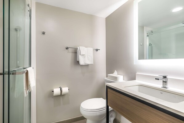 Un baño moderno con cabina de ducha de vidrio, inodoro, lavamanos con espejo y toallero.