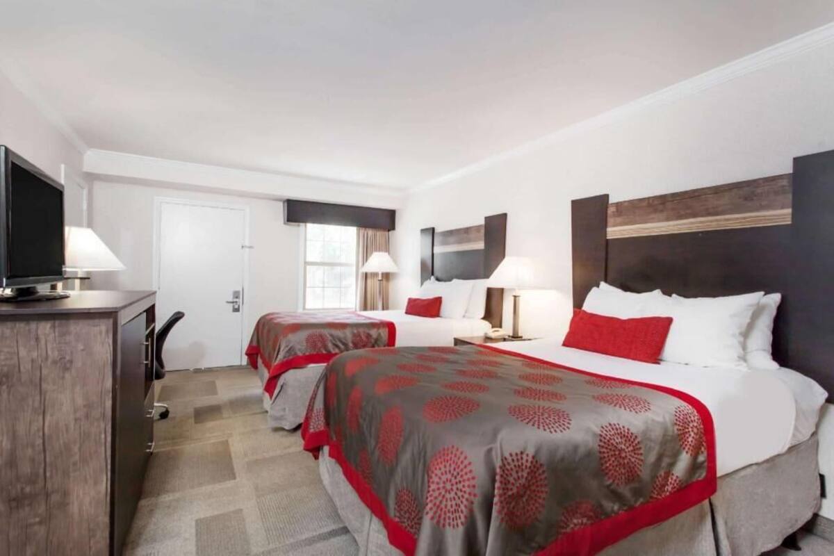 A hotel room with two beds, a desk, and a TV.