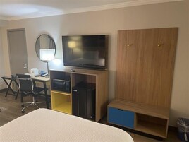 Habitación de hotel con cama, escritorio con silla, televisor, microondas y armario.