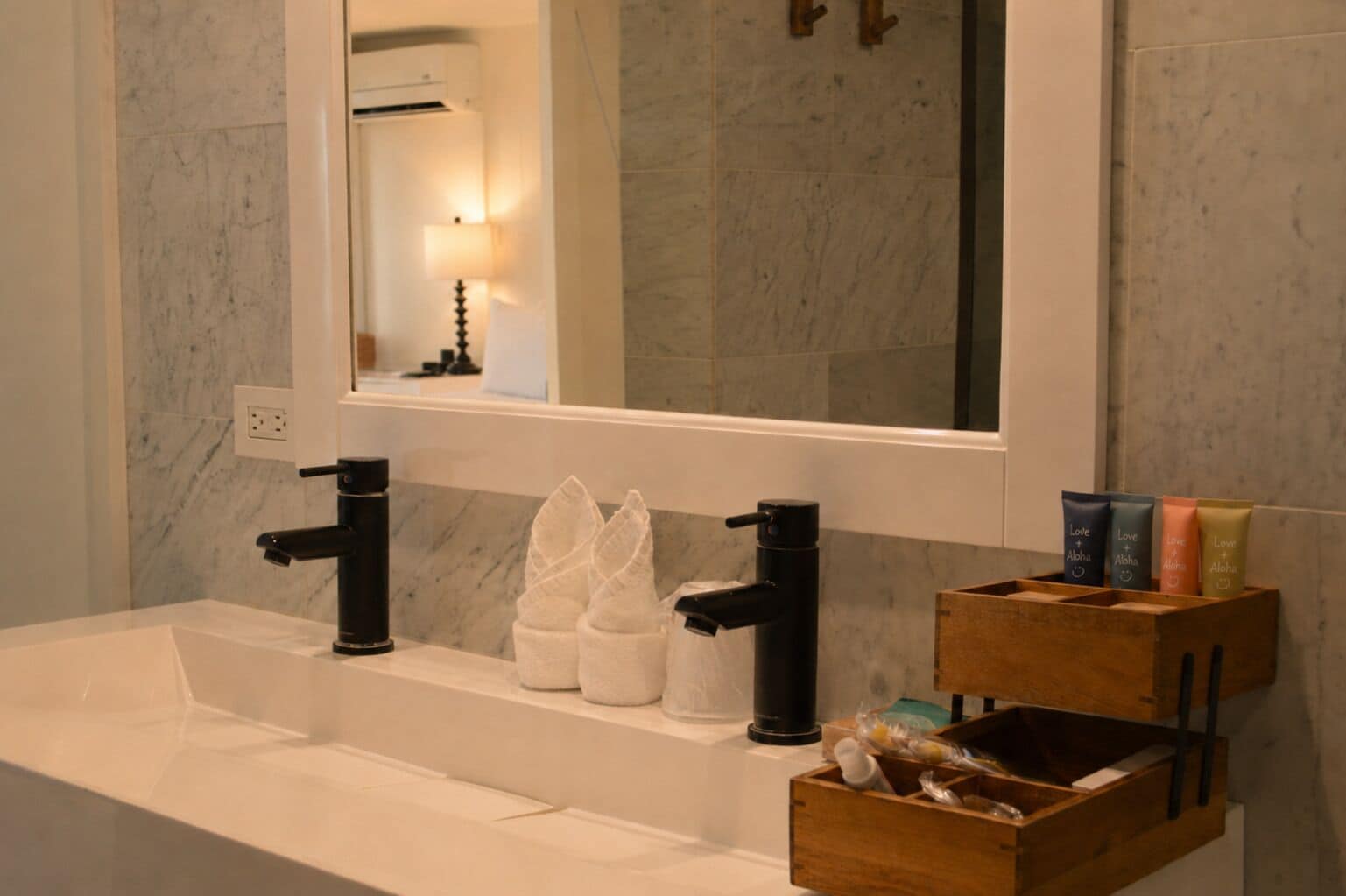 Un baño con un lavabo blanco, grifos negros, un espejo y una caja de madera con artículos de tocador.