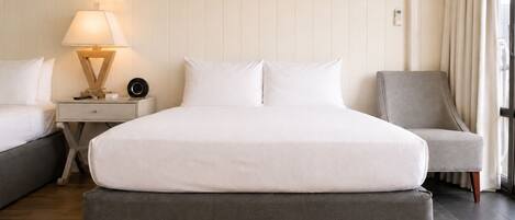 A hotel room with a bed, a bedside table with a lamp, a chair, and an air conditioning unit.