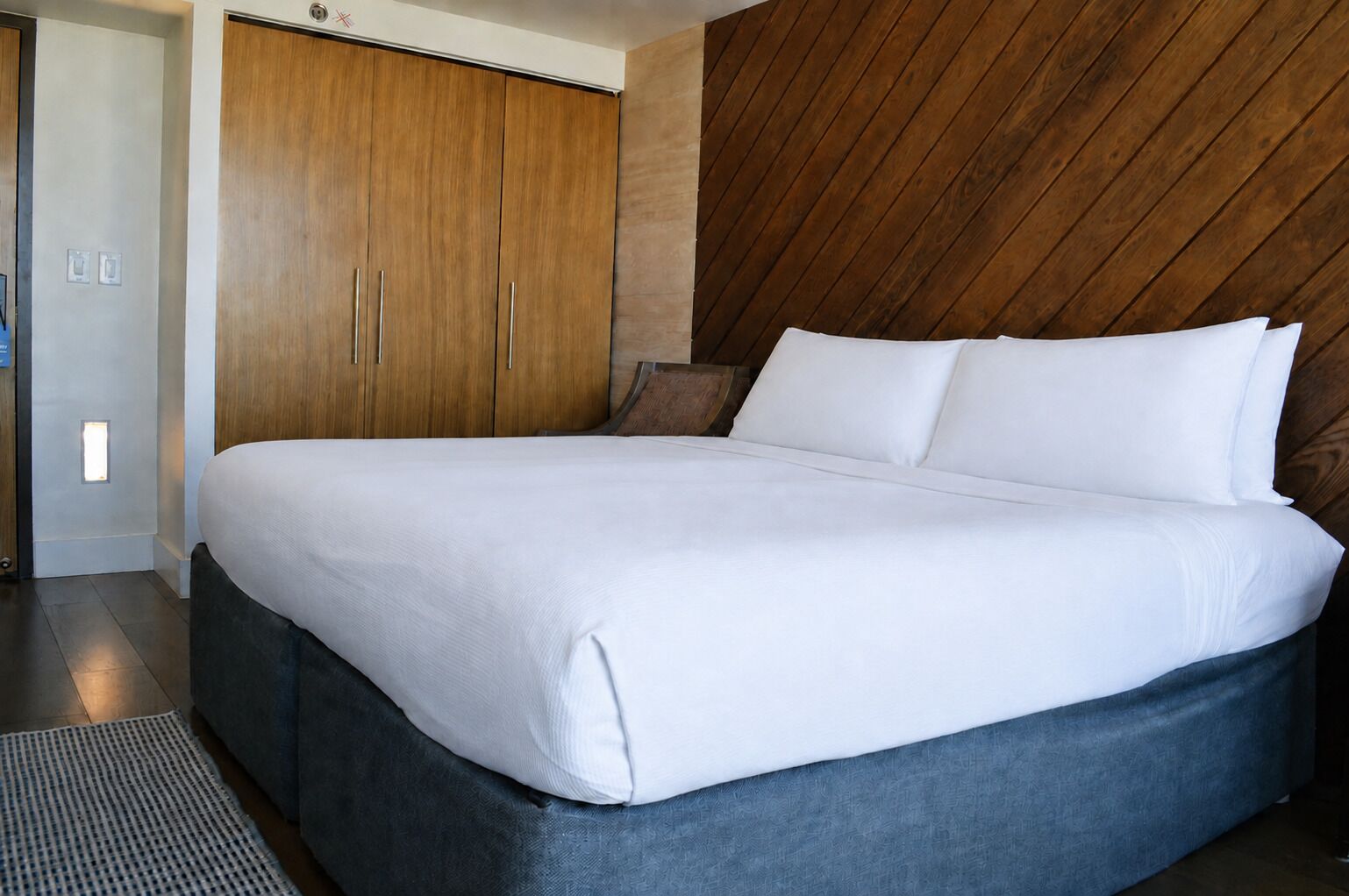 A modern hotel room with a large bed, wooden wardrobe, and a unique wall design.