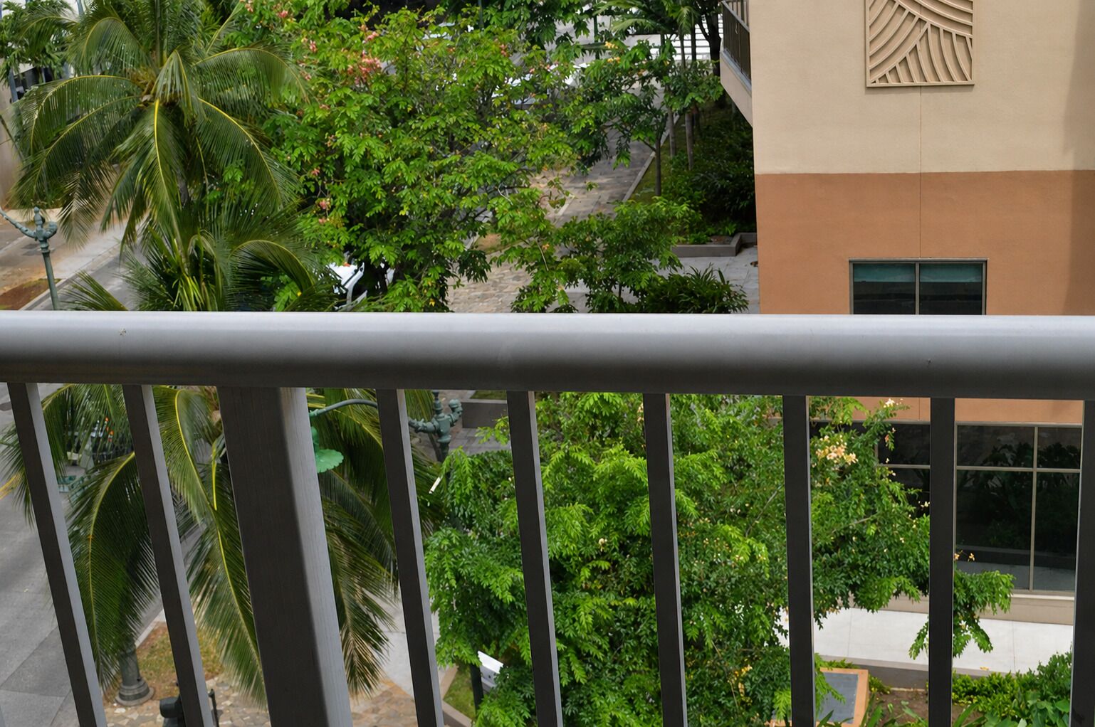 Un balcón con barandilla metálica que da a un área verde exuberante con árboles y un edificio de fachada color beige.
