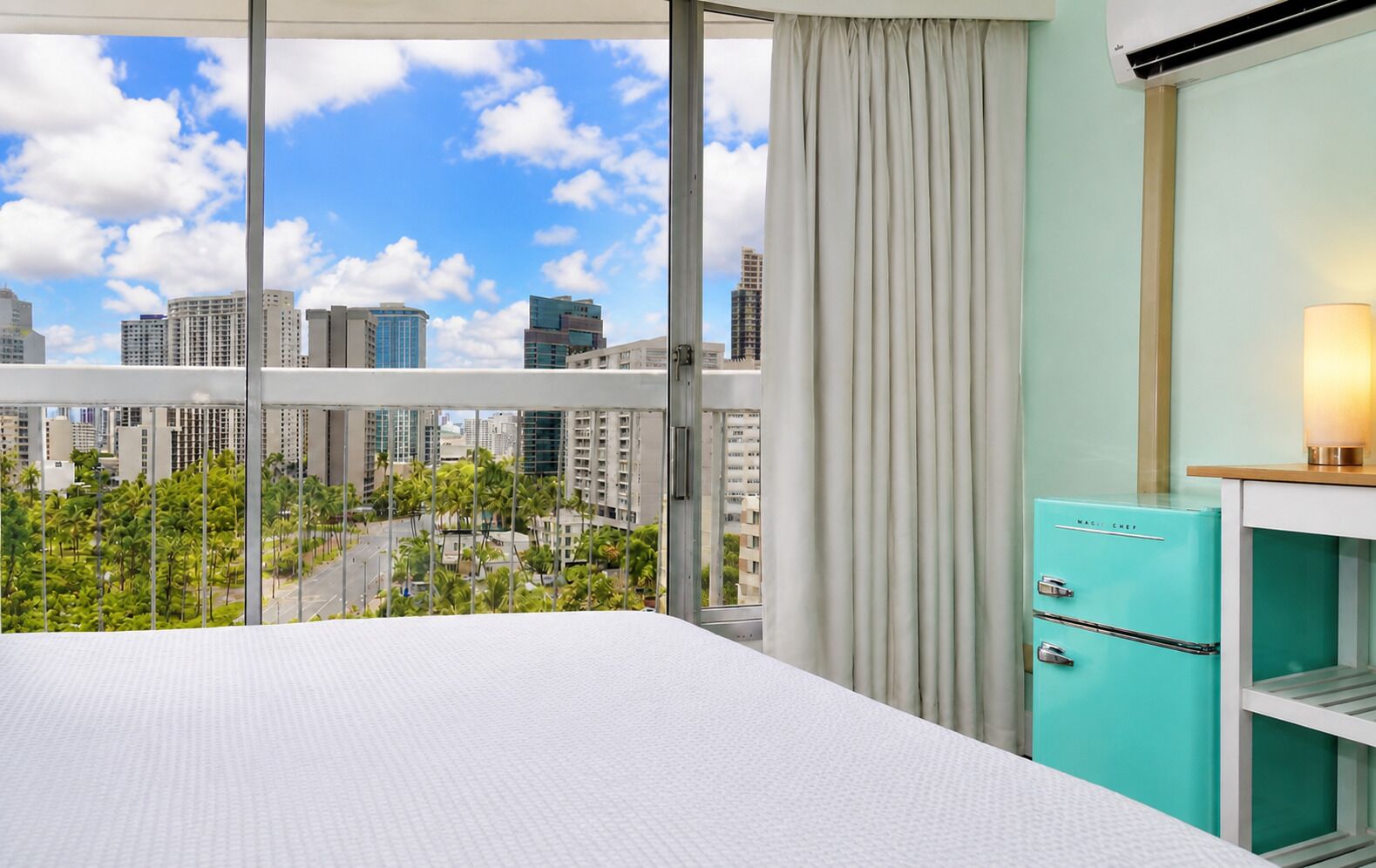 Une chambre d’hôtel avec une grande fenêtre, un lit, un minibar et une vue sur le paysage urbain.