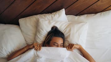 Una persona acostada en una cama con ropa blanca y techo de madera.