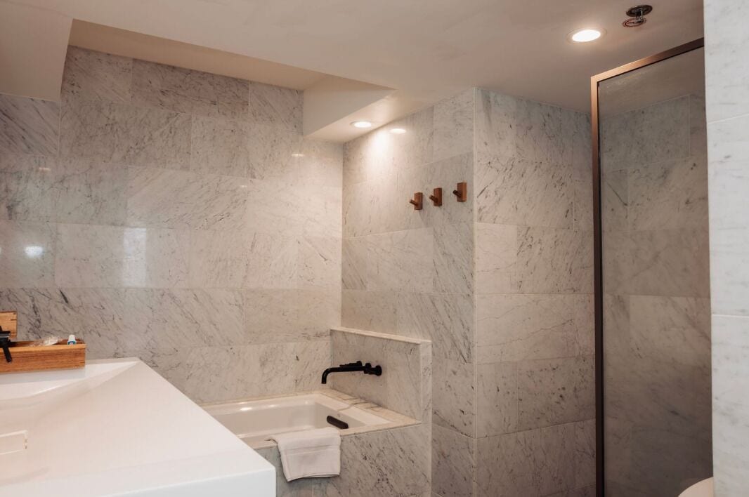 A modern bathroom with a marble wall, a white sink, a black faucet, and a glass shower enclosure.
