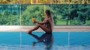 A person sitting by a pool with a drink, surrounded by greenery and palm trees. - Hotel La Croix (Honolulu)