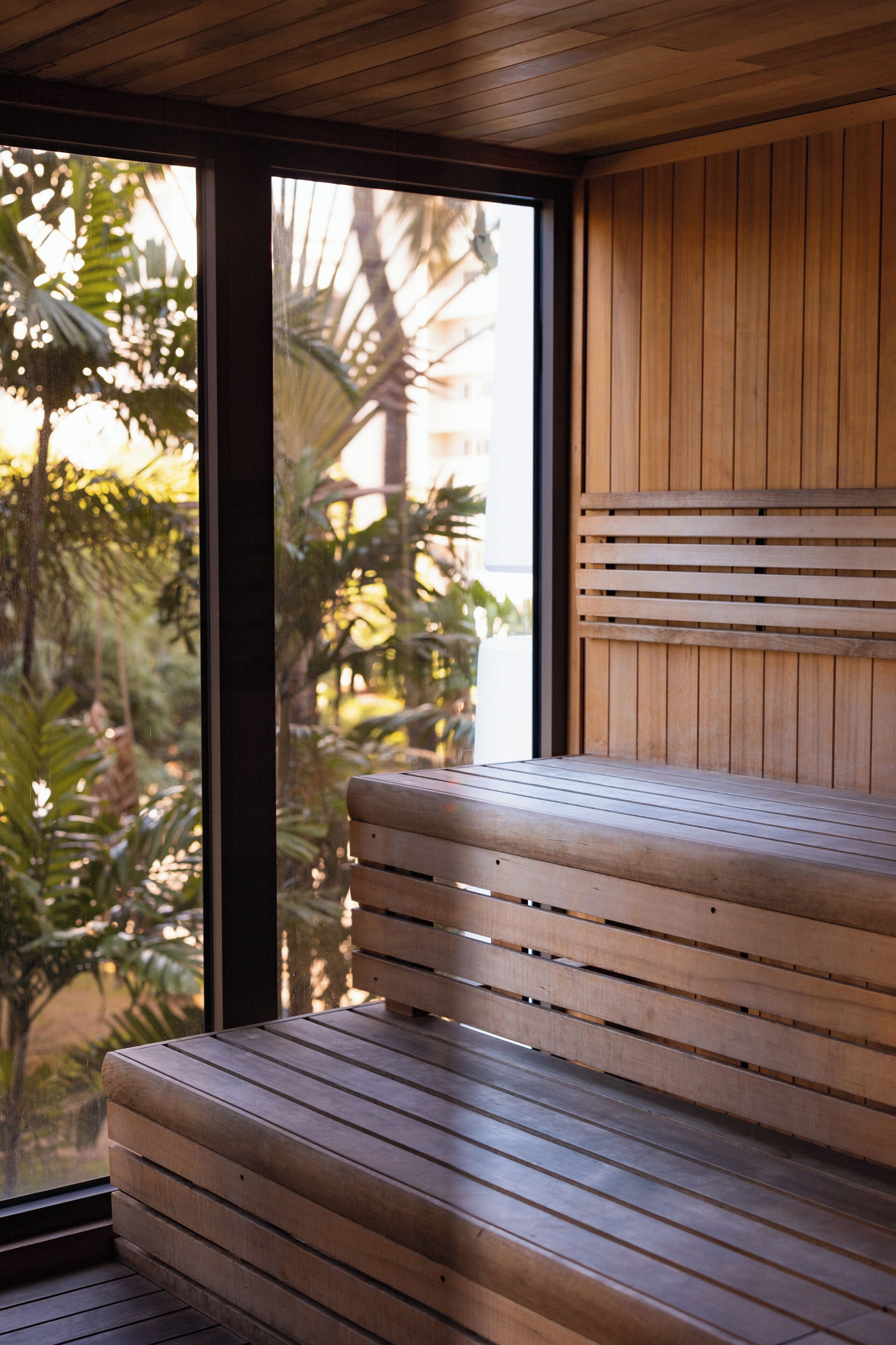 Un banc en bois, doté d’assises composées de lattes horizontales, est placé devant une fenêtre donnant sur un paysage verdoyant.