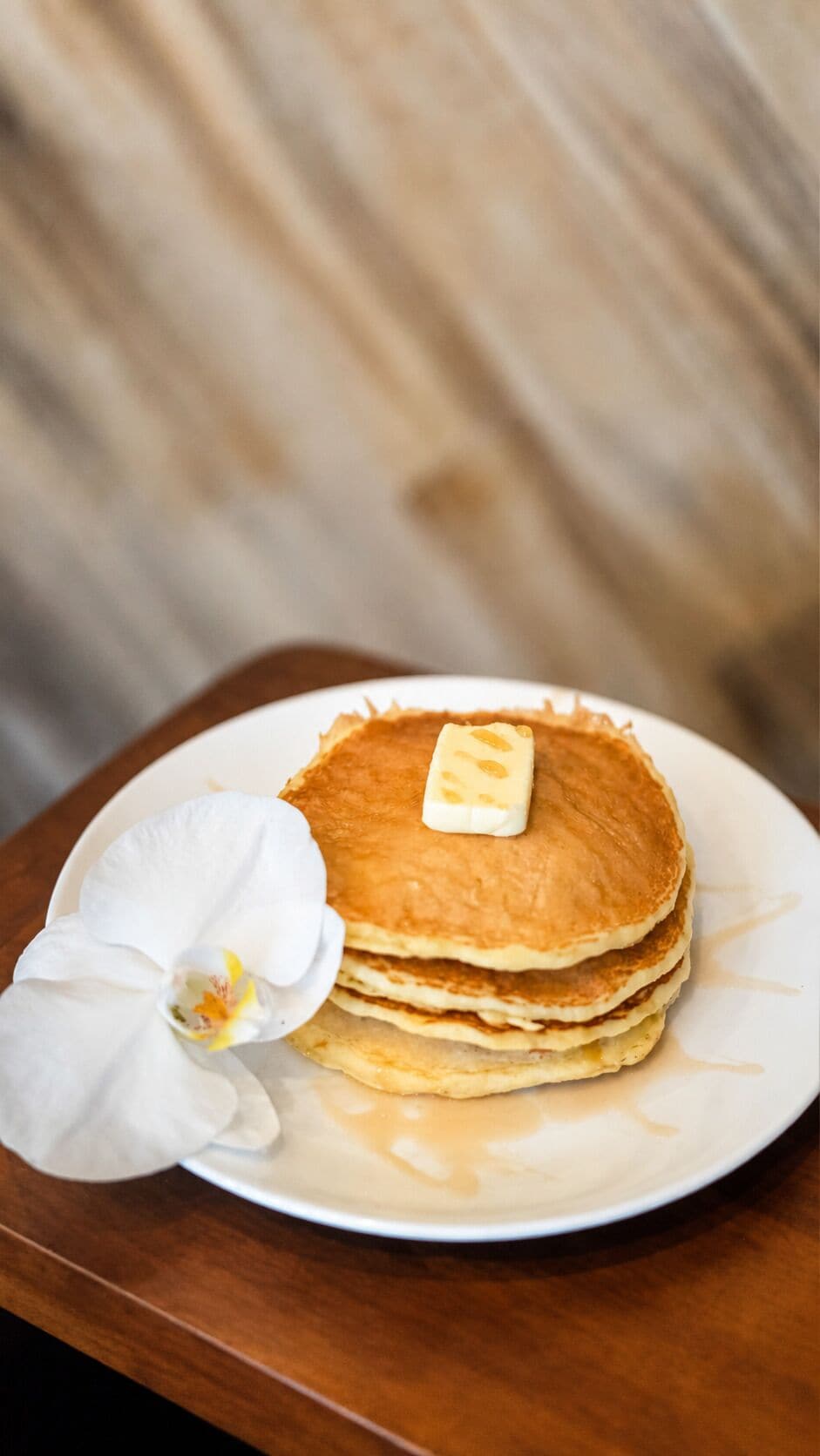 A stack of pancakes on a white plate with a butter knife, accompanied by a white orchid.
