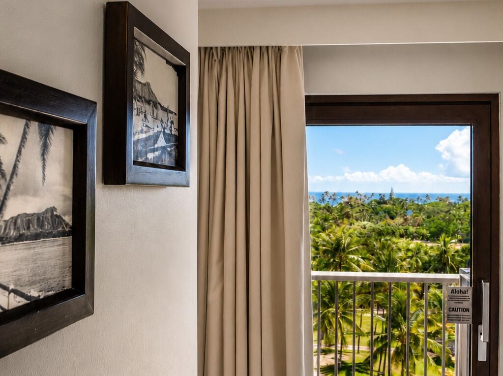 Habitación de hotel con vistas a un paisaje tropical, una puerta con un letrero de precaución y dos cuadros en la pared.
