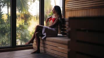 Una persona sentada en un banco de madera junto a un amplio ventanal con vista a la vegetación.