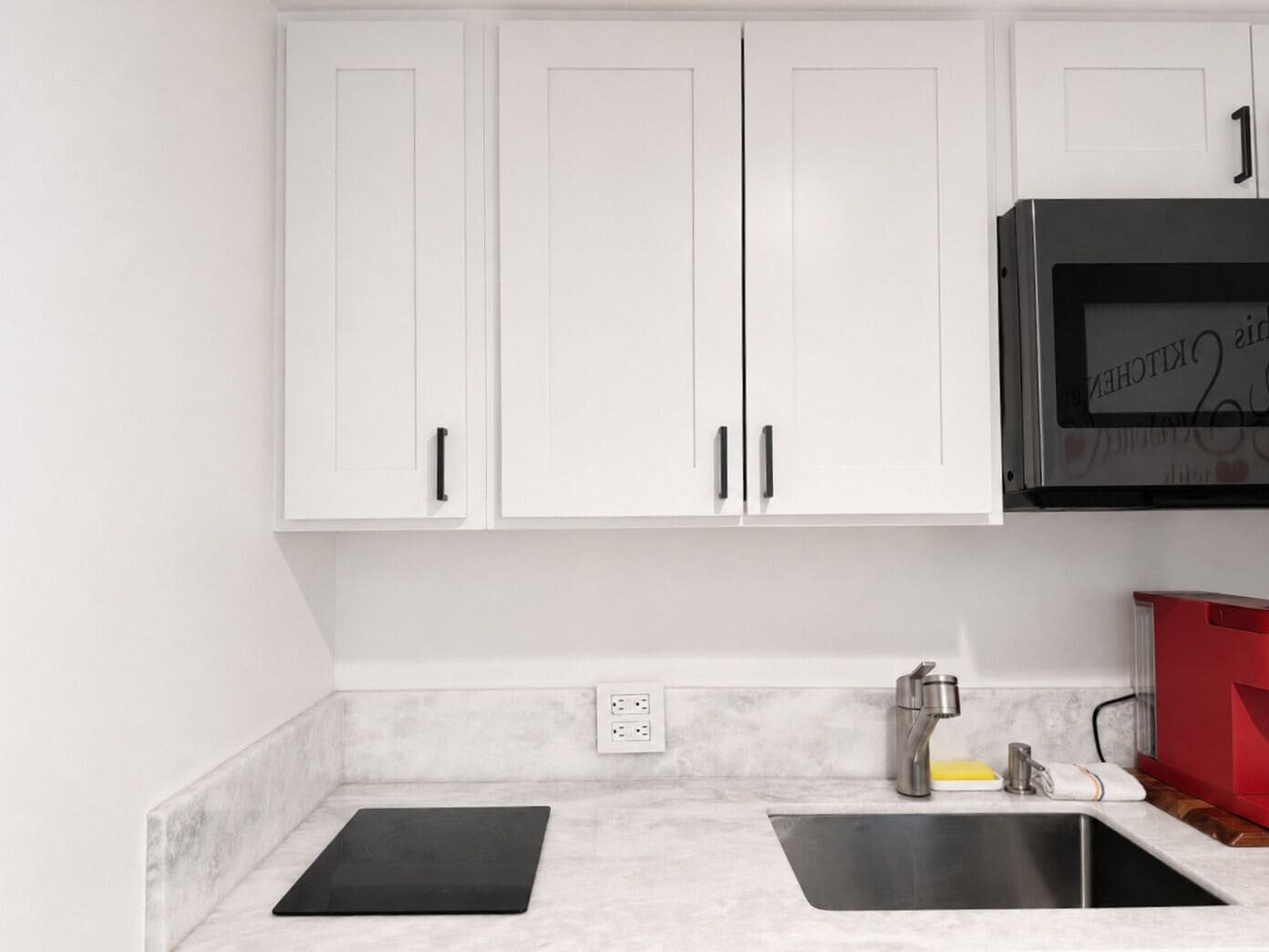 A kitchen with white cabinets, a stainless steel sink, and a black countertop.