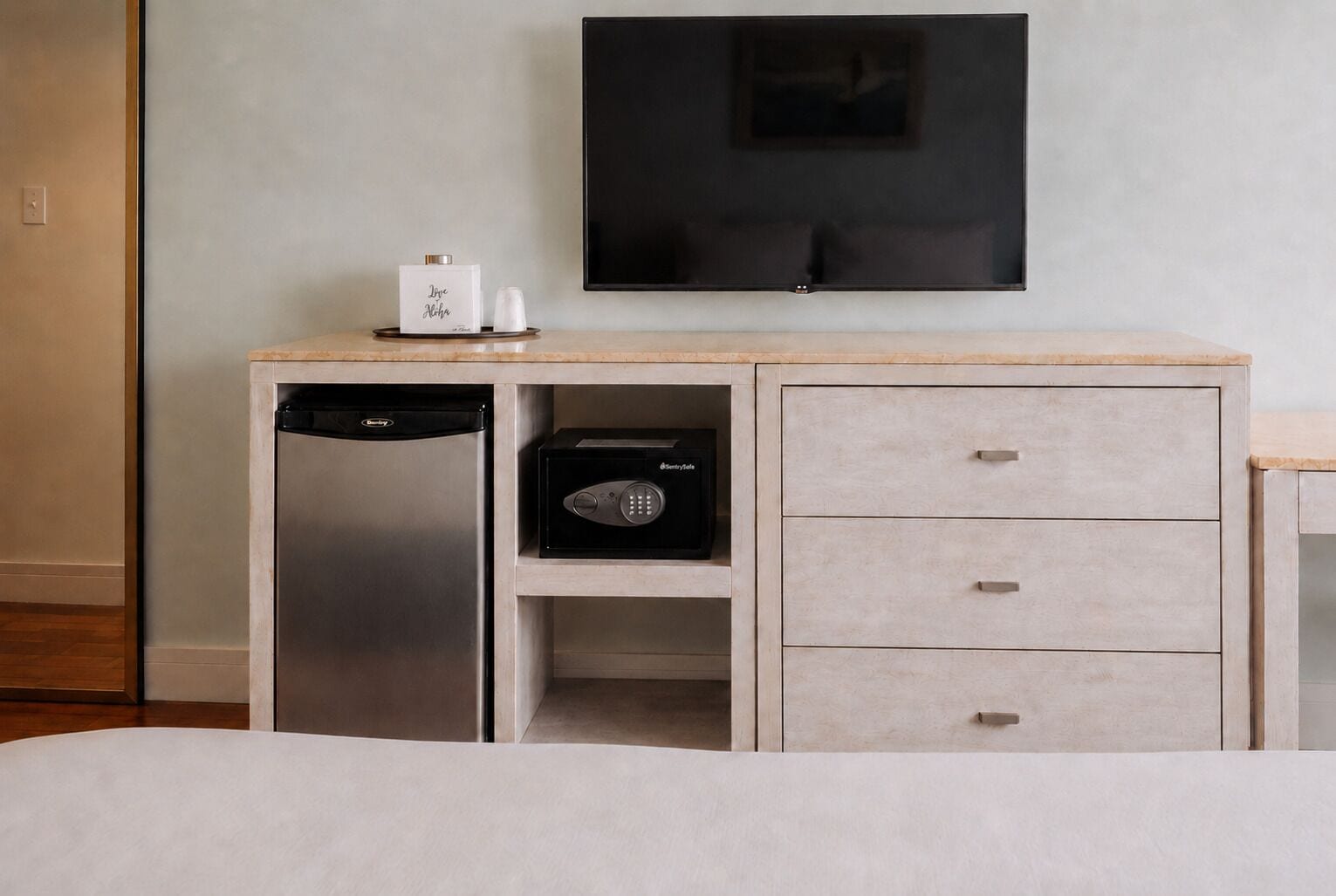 A hotel room with a bed, a wooden desk with a black radio, a white coffee maker, and a black appliance.