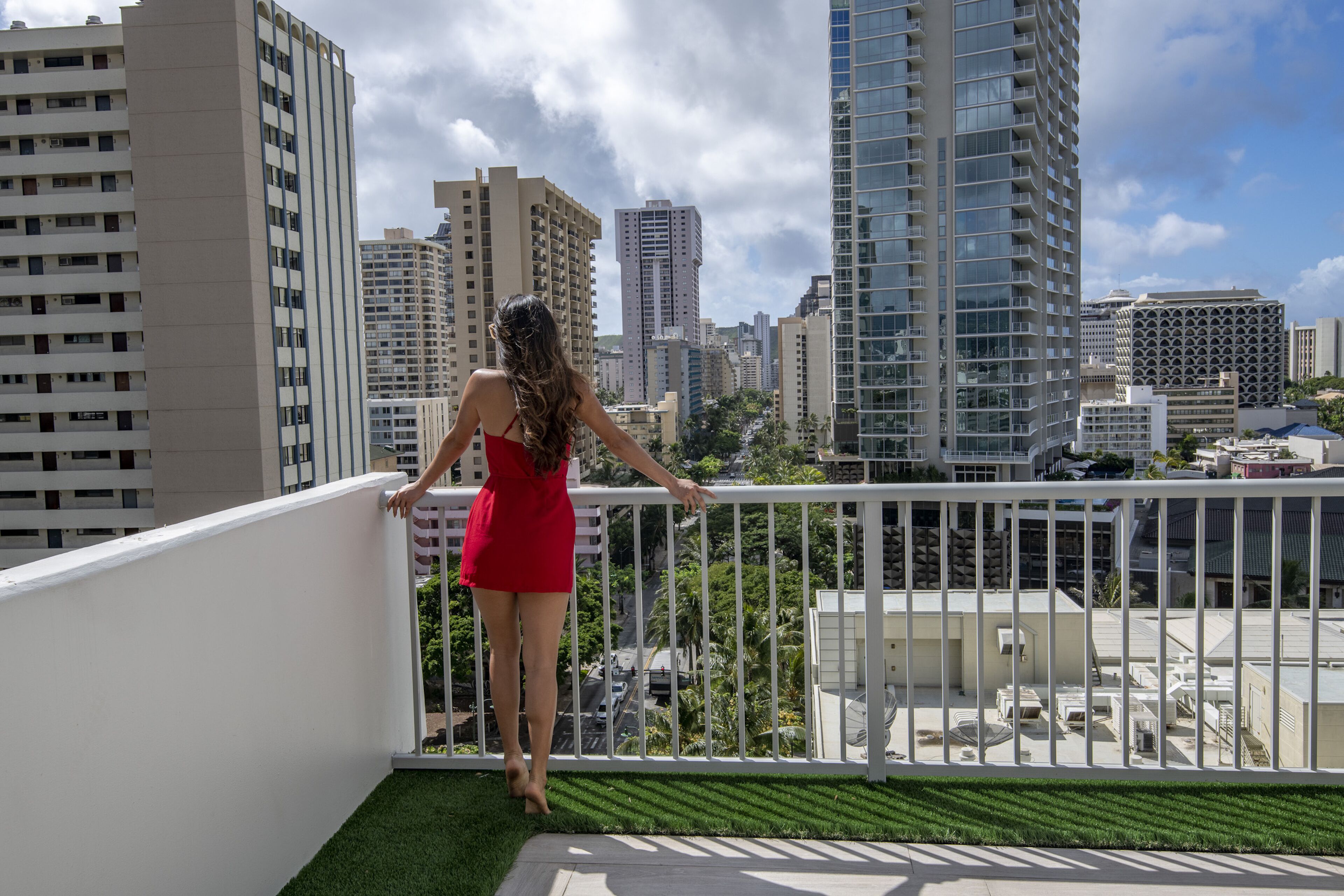 Une femme vêtue d’une robe rouge, debout sur un balcon, avec une vue sur la ville.