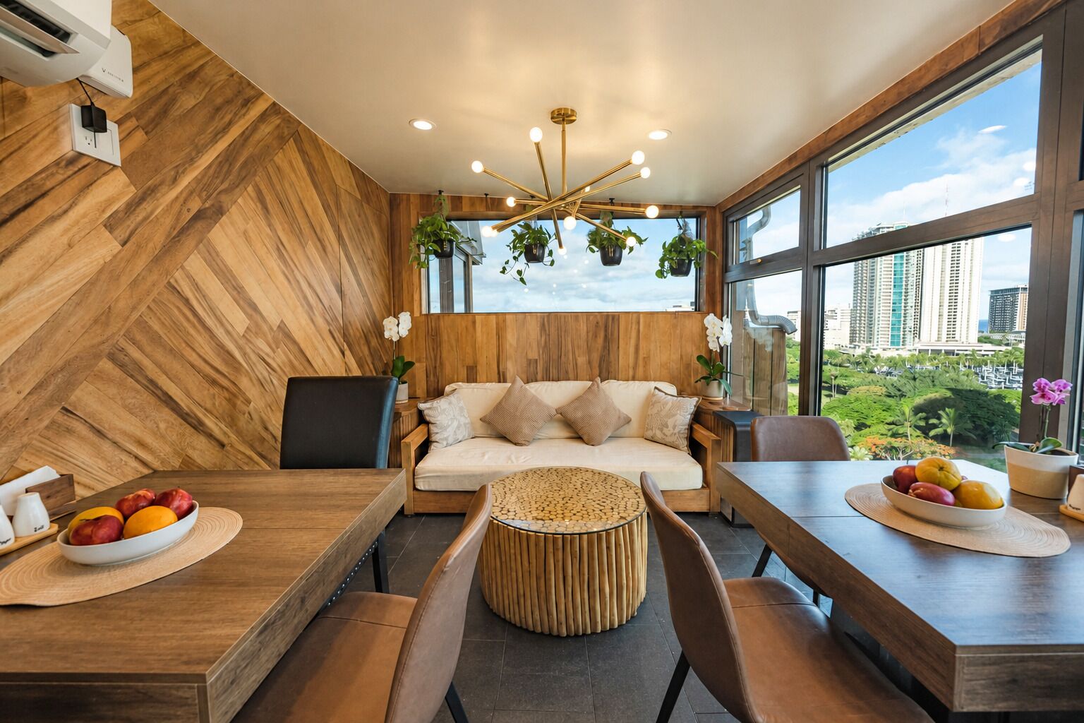 A modern interior with a wooden wall, a sofa, a dining table with fruit, and a view of a cityscape.